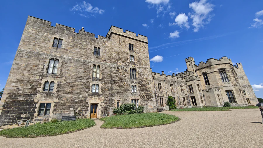 The stone exterior of Raby Castle beneath a bright blue sky