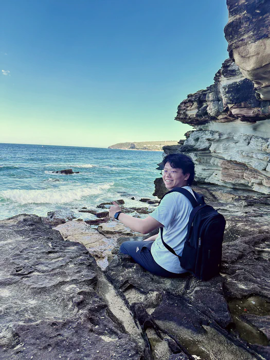 Yixiong Gao sitting on sandstone cliffs beside Manly Beach